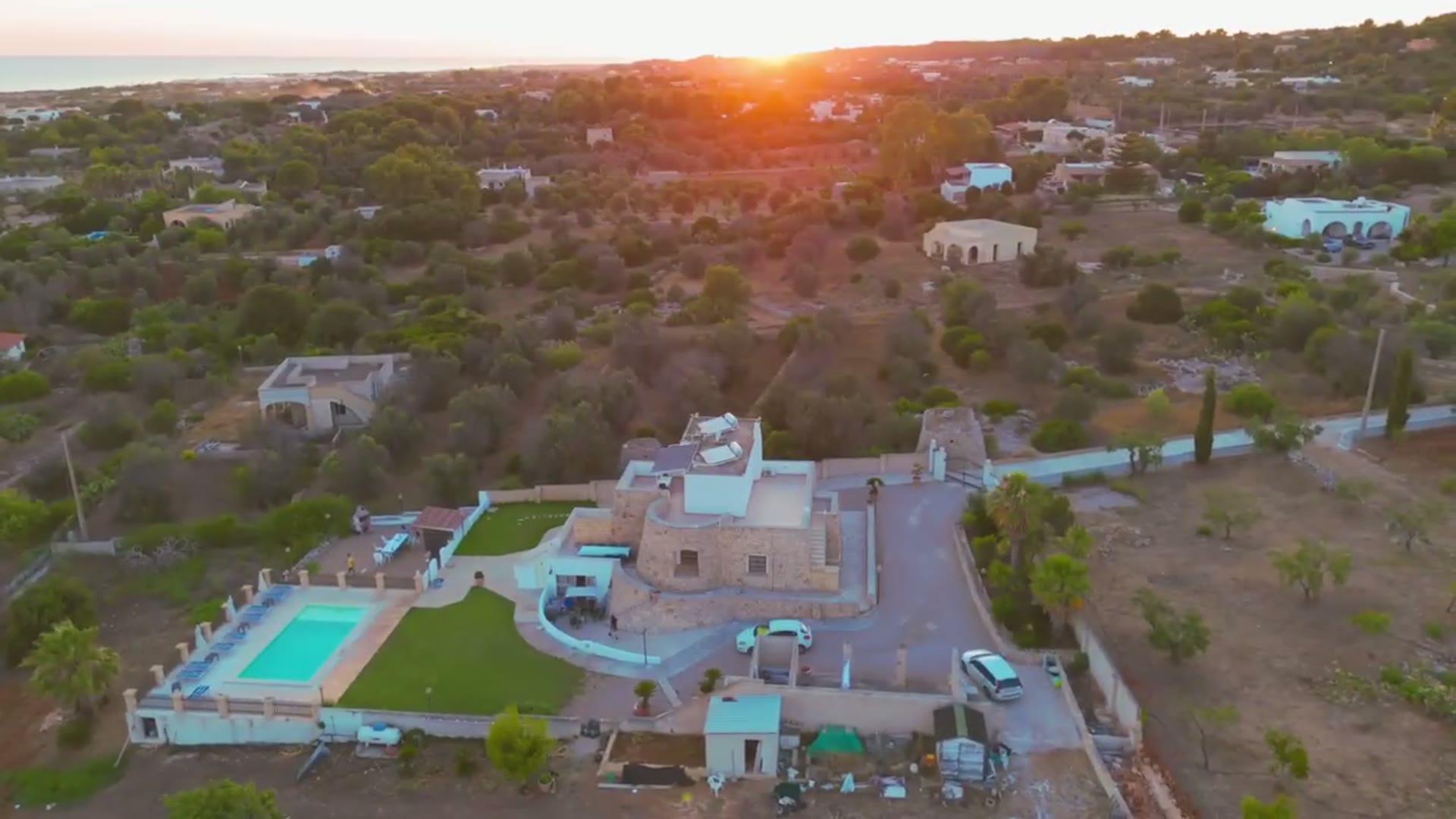 La villa e la piscina con il sole che tramonta dietro gli ulivi
